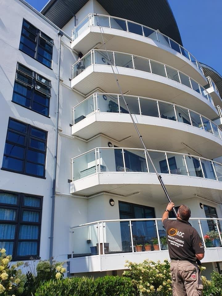 Andy of AOC Window Cleaning in his branded shirt using a water-fed pole on a multi-storey apartment block
