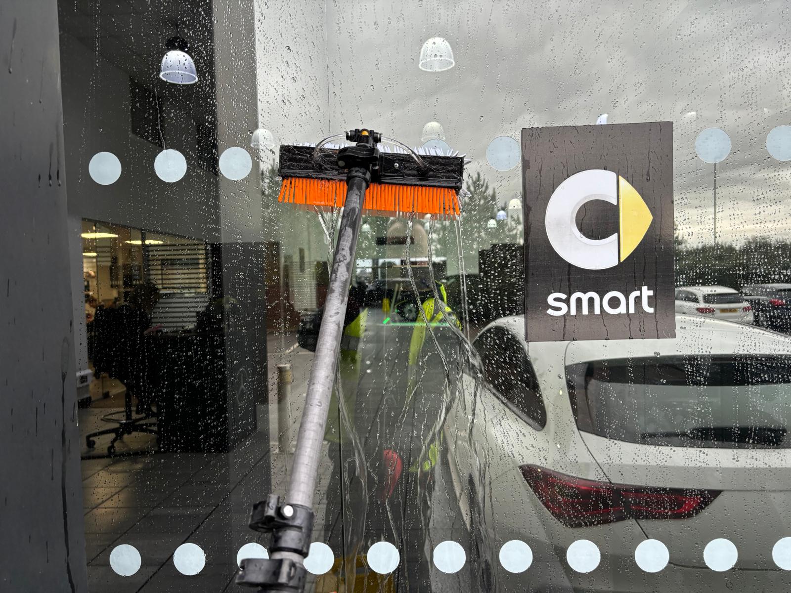 Water-fed pole brush washing showroom glass with pure deionised water running down it